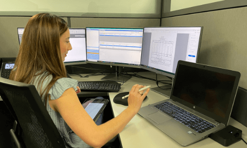woman is typing on multiple monitors to report air emissions on