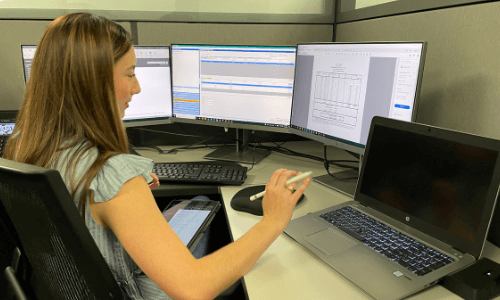 woman is typing on multiple monitors to report air emissions on